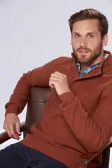 Buzo de tejido grueso color gris, con cuello alto y cierre frontal parcial. Presenta puños y ruedo acanalados, con un diseño de textura tejida en toda la prenda.