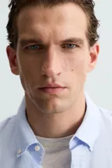 Camisa celeste a rayas verticales, de corte relaxed fit, confeccionada en lino y algodón. Tiene cuello abotonado, manga larga con puños abotonados, bolsillo de parche en el pecho y cierre frontal con botones.