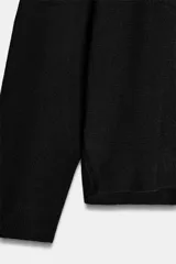 Jersey de punto liso color negro, con cuello subido y mangas largas de diseño murciélago con sisa ancha que se estrecha hacia la muñeca.