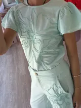 Blusa de lino color celeste con bordado en relieve de formas orgánicas y terminaciones desflecadas en las mangas.
