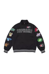 Campera tipo buzo con cierre frontal completo, confeccionada en algodón negro. Presenta cuello alto, puños y ruedo con franjas blancas y múltiples parches bordados con motivos deportivos y gráficos en ambas mangas y pecho.