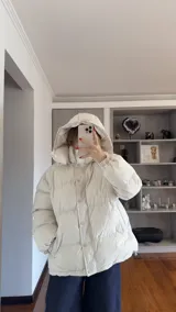 Campera puffer de corte holgado en color beige, con diseño acolchado, cuello alto y capucha desmontable. Cuenta con cierre frontal y botones a presión, además de puños elásticos.