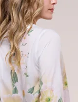 Blusa de silueta holgada y corte recto con caída fluida, escote redondo y mangas largas con puños anchos estructurados, con estampado floral en tonos pasteles sobre fondo blanco.