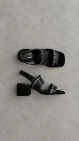 Sandalias de cuero marrón con punta cuadrada, tiras texturizadas con detalles de ojales metálicos y cordones entrelazados, y tira ajustable con velcro en el talón.