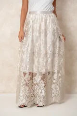 Pollera larga de tul con bordados florales en tono crema. Posee un forro interno opaco que llega hasta la rodilla, creando un efecto de transparencia en la parte inferior.