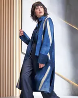 Tapado largo azul con rayas verticales color crema, cuello alto que se prolonga como un cinturón, aberturas laterales y bolsillos.