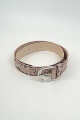 Cinturón de cuero sintético color rosado con efecto desgastado, decorado con tachas metálicas circulares y en forma de estrella. Cuenta con hebilla metálica plateada de diseño clásico.