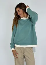 Sweater verde de punto, con cuello redondo y mangas largas. Presenta un diseño holgado y bordes acanalados en cuello, puños y dobladillo.