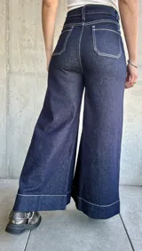 Pantalón de jean azul oscuro, de corte ancho, con bolsillos delanteros cuadrados y costuras blancas contrastantes.