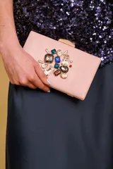 Clutch rígido de color rosado con apliques de piedras facetadas de diversos colores y cierre metálico dorado en la parte superior.