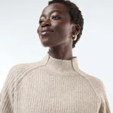 Sweater de punto canalé en color beige, con cuello alto y mangas largas con puños ajustados.
