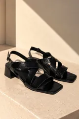 Sandalias de cuero vacuno color negro con acabado efecto craquelado. Presentan diseño de tiras cruzadas en el empeine, puntera cuadrada, taco cuadrado y tira ajustable al talón con hebilla metálica.