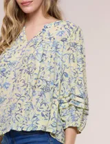 Blusa holgada de gasa estampada en tonos amarillos y azules, con cuello en V, mangas 3/4 abullonadas y alforzas horizontales.