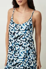 Vestido corto sin mangas con tirantes finos, escote redondo y diseño estampado en tonos azul, negro y blanco, con detalle de volados en el borde inferior.