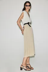 Vestido midi bicolor con parte superior blanca de escote en V cruzado con ribete negro y falda plisada en color tostado. Cuenta con mangas sisa, cintura elástica y un cinturón negro tipo reptil con hebilla ovalada.