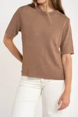 Sweater de tejido de punto fino en color arena, con cuello redondo y mangas cortas. Presenta un diseño minimalista con un pequeño detalle metálico en el ruedo.