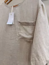 Blusa de lino color blanco, con escote redondo, mangas cortas amplias, calce relajado y un bolsillo delantero con detalle de lentejuelas.