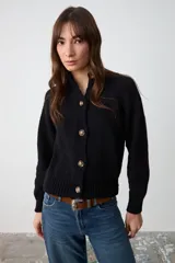 Cardigan de punto negro con cuello camisero, cierre frontal de botones y mangas largas con puños acanalados.