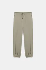 Pantalón de tiro medio color verde oliva, estilo bombacho o jogger, con cintura ajustable mediante cordón y puños elásticos con botón en los tobillos.