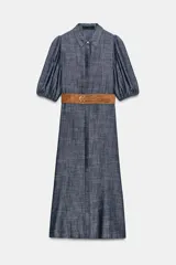Vestido midi de denim azul con cuello camisero, mangas abullonadas y cierre frontal oculto con botones. Incluye un cinturón marrón con hebilla metálica.