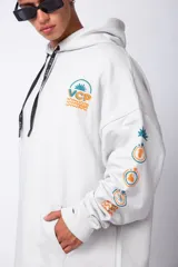 Buzo canguro oversize de algodón rústico, color gris claro, con capucha y cordones ajustables con logo estampado. Presenta un diseño gráfico pequeño en el pecho y detalles estampados en la manga.