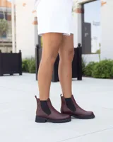 Botas tipo Chelsea de cuero color marrón, con paneles elásticos laterales en color negro y suela de goma dentada en color negro. Presenta un detalle de tirador en la parte trasera en gamuza color tostado.