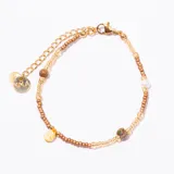 Pulsera de cadena dorada con cuentas pequeñas de color dorado y bronce, intercaladas con piedras naturales y una perla blanca. Incluye dije redondo con logo grabado.