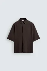 Camisa de corte relajado confeccionada en tejido mezcla de lyocell, color marrón oscuro. Presenta cuello bowling, manga corta y cierre frontal con botonadura oculta por solapa.