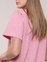 Blusa blanca de textura gofrada, de corte recto y semi holgado, con mangas cortas y escote redondo adornado con un canesú frontal en crochet calado.