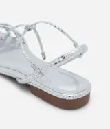 Sandalia plana marca Satinato, color dorado metalizado con textura tipo croco. Posee tiras finas con detalle de nudo en el empeine y cierre de lazo ajustable al tobillo. Diseño de puntera redonda y suela plana.