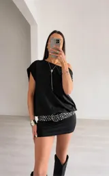 Vestido corto negro de estilo asimétrico con un hombro al descubierto, corte holgado en la parte superior y ajustado en la falda. Incluye un cinturón negro con ojales metálicos plateados.