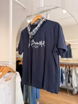 Remera azul marino de manga corta y corte clásico, con estampa bordada con la palabra "Beautiful" en el frente. Incluye un pañuelo de cuello con estampado a cuadros en tonos oscuros.