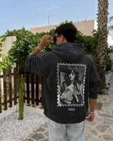 Canguro con capucha de algodón y poliéster, color negro con efecto acid wash, corte regular fit y estampa en la espalda con diseño en blanco y negro de una persona con un gato dentro de un sello postal, acompañada de texto en celeste.