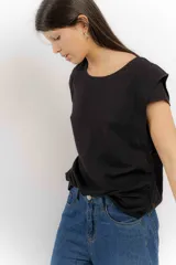 Remera sin mangas de corte holgado, con hombreras marcadas que crean un efecto de manga corta estructurada. Presenta un diseño minimalista con frunces laterales en la cintura y cuello redondo.