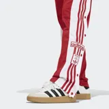 Pantalon deportivo Adidas modelo Adibreak, color rojo con franjas laterales blancas y botones a presión. Presenta cintura elástica y corte holgado.