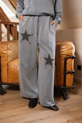 Pantalón gris de corte amplio y fluido, con bolsillos laterales y apliques de estrellas negras con contorno dorado en ambas piernas.