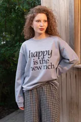 Buzo de cuello redondo gris melange con estampa frontal en negro con la frase "happy is the new rich".