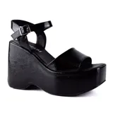 Sandalias negras de plataforma con taco corrido, tira ancha sobre los dedos y pulsera al tobillo con hebilla metálica.