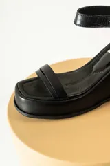 Sandalias negras de cuero sintético con plataforma y taco de cuña. Tienen dos tiras en el empeine y una tira con hebilla alrededor del tobillo.