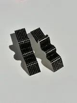 Par de aros colgantes con forma geométrica irregular, recubiertos de strass negros sobre base plateada.