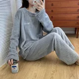 Conjunto de pijama de dos piezas confeccionado en tela de plush texturizada con diseño de rayas verticales en relieve. Incluye una remera de manga larga con cuello redondo y un pantalón de corte holgado. La remera presenta un pequeño bordado decorativo en el pecho.