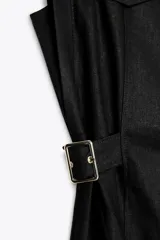 Vestido midi blanco, sin mangas, con cuello solapa y escote pico. Presenta falsos bolsillos con solapas en el pecho, trabillas con hebillas en la cintura y cierre frontal de botones.