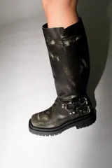 Bota alta estilo biker de cuero marrón con efecto desgastado, suela track de goma y detalles de hebillas metálicas en el tobillo y en la parte superior de la caña.