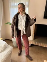 Camisa de color marrón chocolate, confeccionada en tela liviana y fluida. Presenta un diseño con múltiples vuelos frontales, cuello con lazo para anudar y mangas largas abullonadas con puños ajustados.