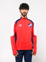 Buzo de entrenamiento Umbro del Club Nacional de Football, con cierre frontal parcial y cuello alto. Presenta un diseño en bloques de color rojo, blanco y azul marino, con el escudo del club y el logo de la marca en el pecho.