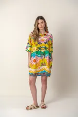 Camisola de manga corta con cuello camisero y cierre frontal de botones. Presenta un estampado colorido con motivos tropicales, palmeras y elementos abstractos sobre fondo amarillo.