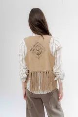 Chaleco de gamuza sintética color beige, con diseño abierto sin cierre. Presenta detalles de tejido de punto calado en los paneles frontales y flecos largos en el ruedo.