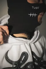 Hoodie blanco con pasamontañas negro incorporado, corte oversize, estampado en el pecho y mangas, y bolsillo tipo canguro.