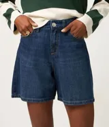 Bermuda de jeans azul oscuro, con trabillas en la cintura, bolsillos laterales y traseros, y cierre de botón y cremallera.