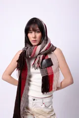 Bufanda de lana merino tejida en telar, con diseño de rayas en tonos marrón, beige y rojo. Presenta flecos en los extremos y un parche negro con la palabra "CAPER" en blanco.